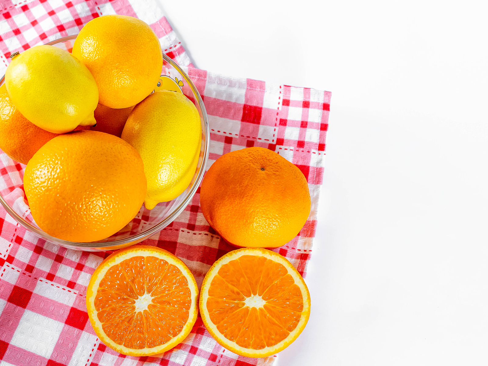 Спелые апельсины и лимоны в стеклянной миске на столе
