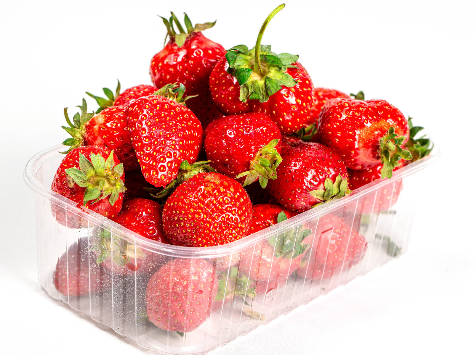 Спелая вкусная клубника в пластиковом контейнере на белом фоне