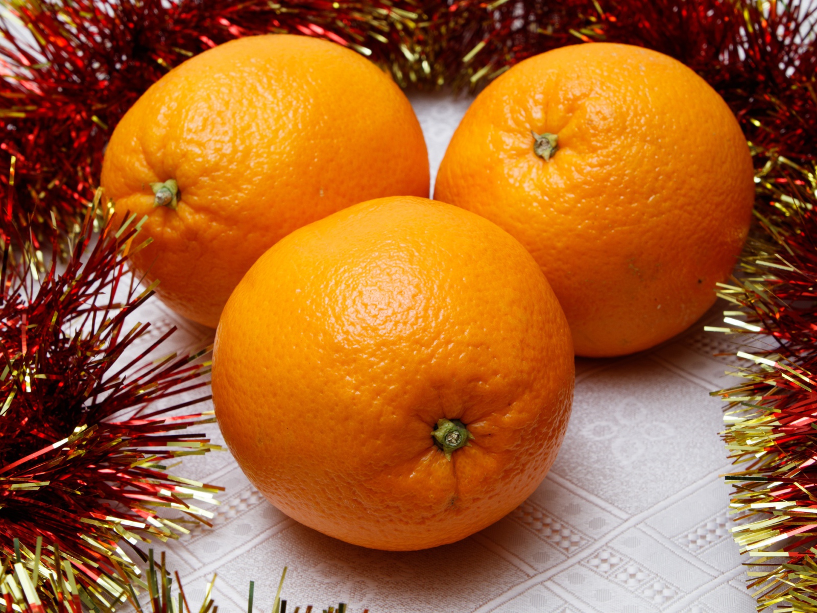 Три больших апельсина на столе с мишурой 
