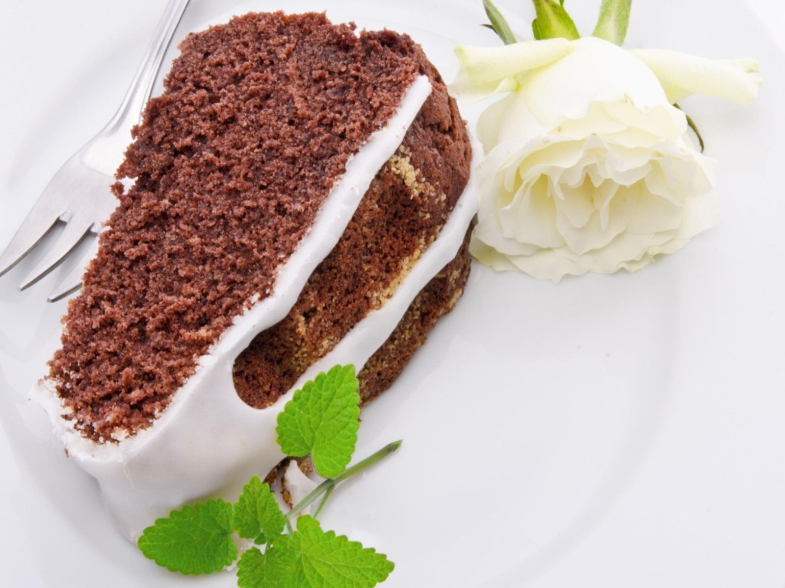 Кусок шоколадного пирога на тарелке с белой розой 