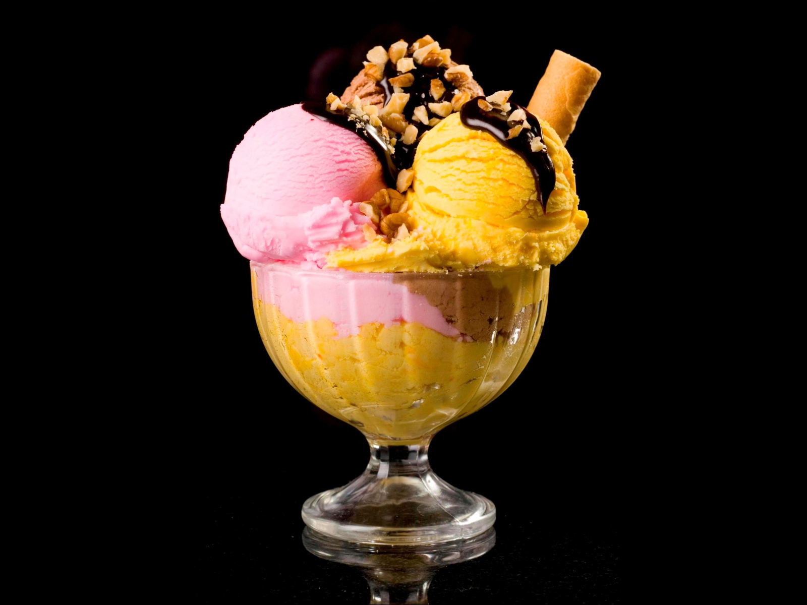 Шарики фруктового мороженого в креманке с орехами и шоколадом на черном фоне