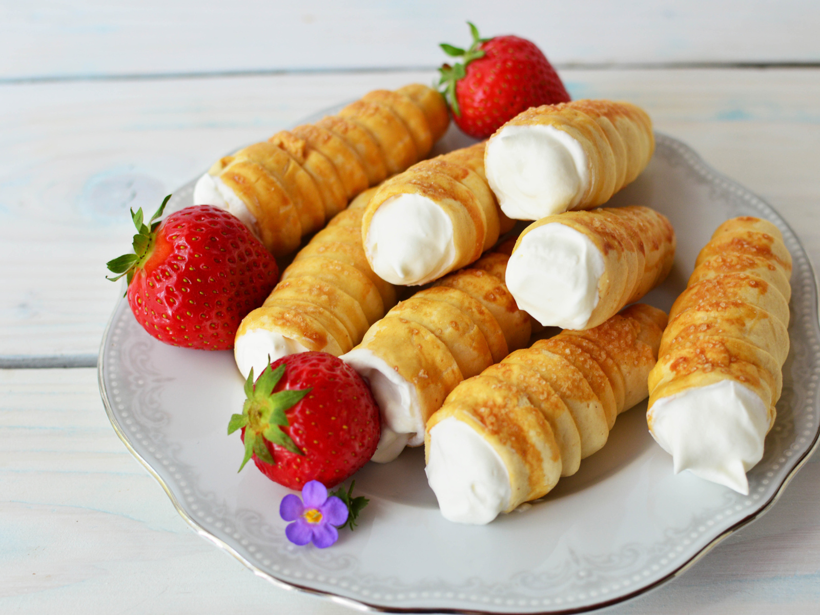 Пирожные трубочки с кремом и ягодами клубники на тарелке 