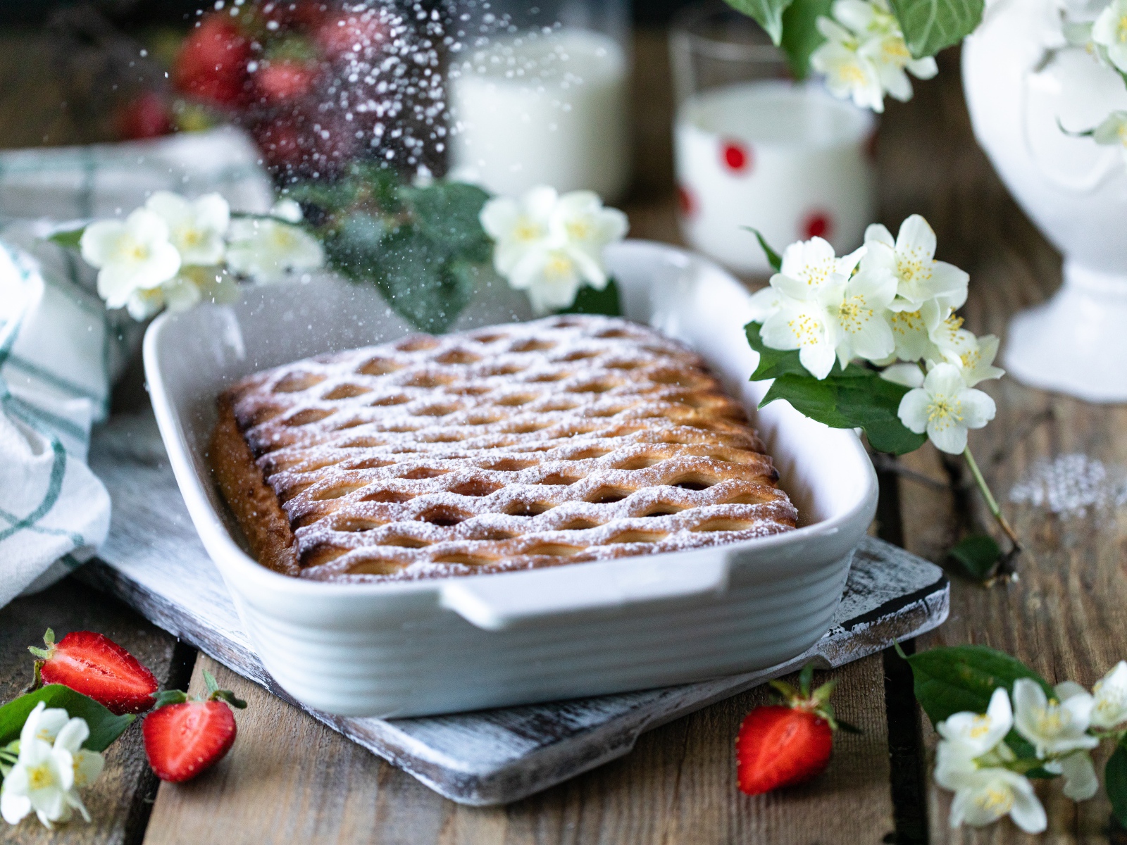 Вкусный клубничный пирог с сахарной пудрой на столе с цветами жасмина