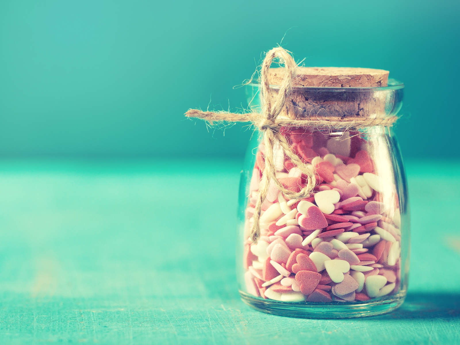 Glass jar with small heart shaped candies on blue background