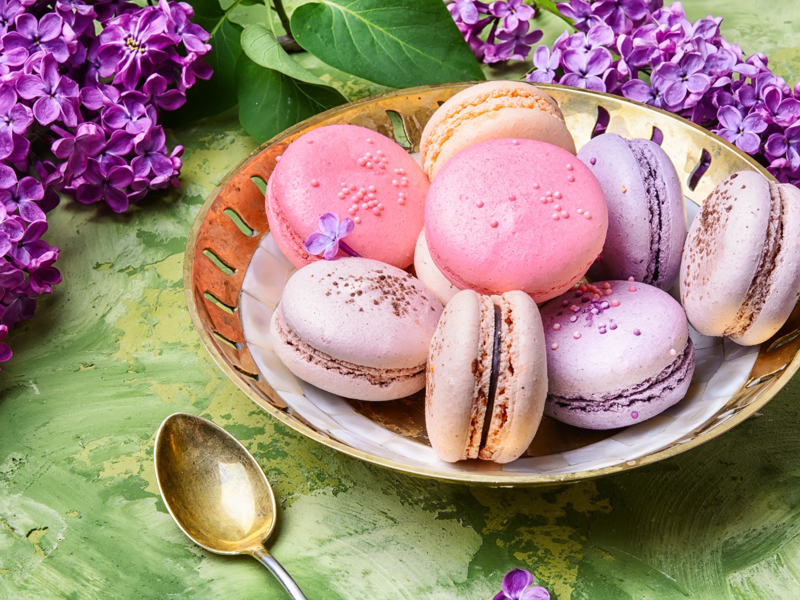 Разноцветный десерт макарон в тарелке на столе с цветами сирени 