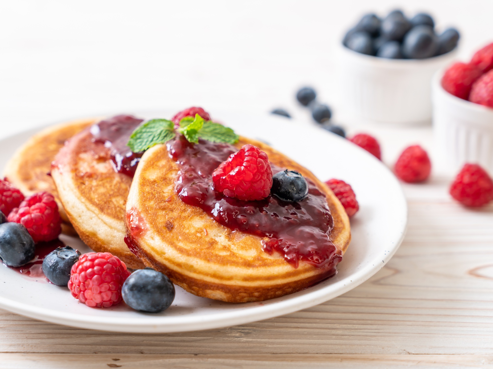 Румяные оладьи с джемом на тарелке с ягодами черники и малины