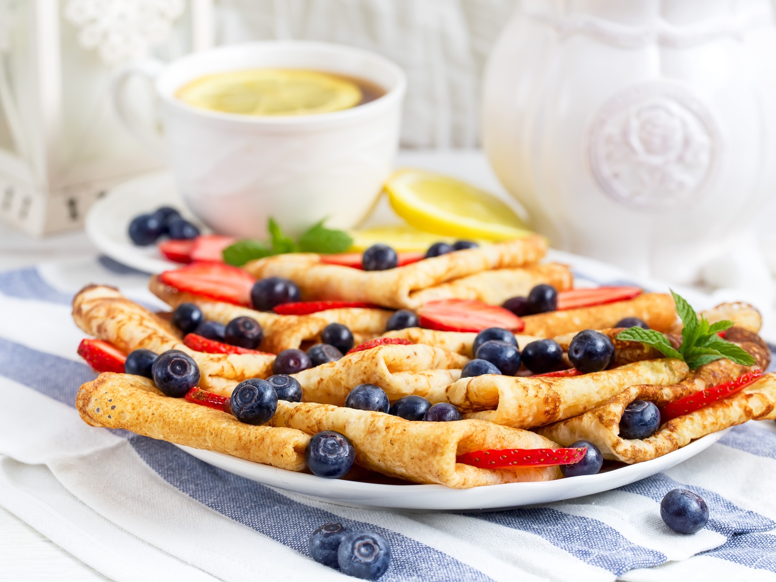 Тонкие блинчики с ягодами черники и клубники на столе с чаем