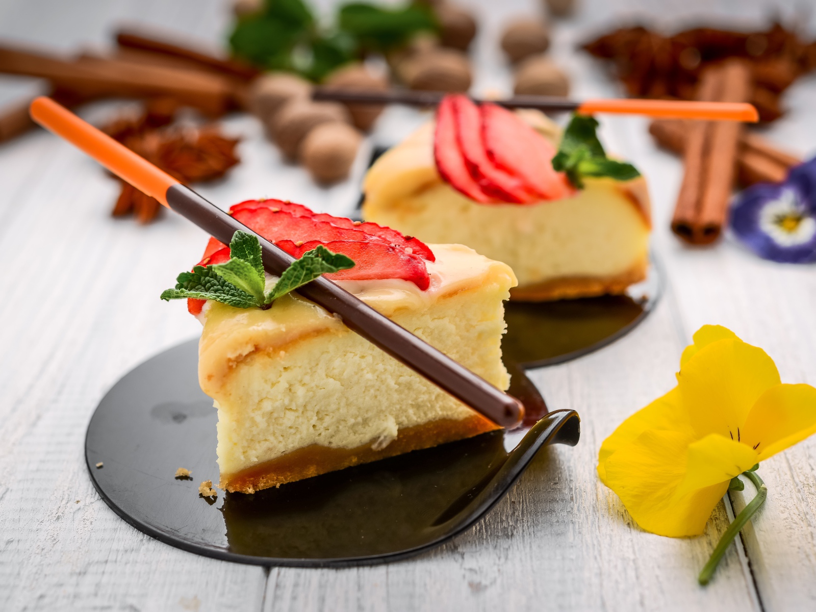 Два куска чизкейка с клубникой на столе с палочками