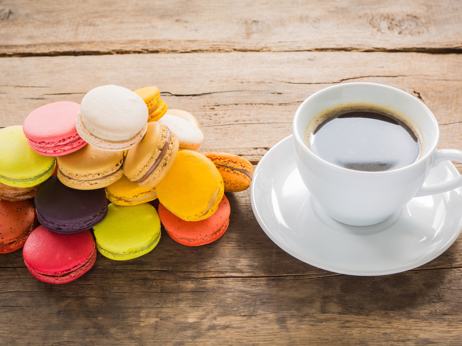 Белая чашка кофе на столе с разноцветным десертом макарун