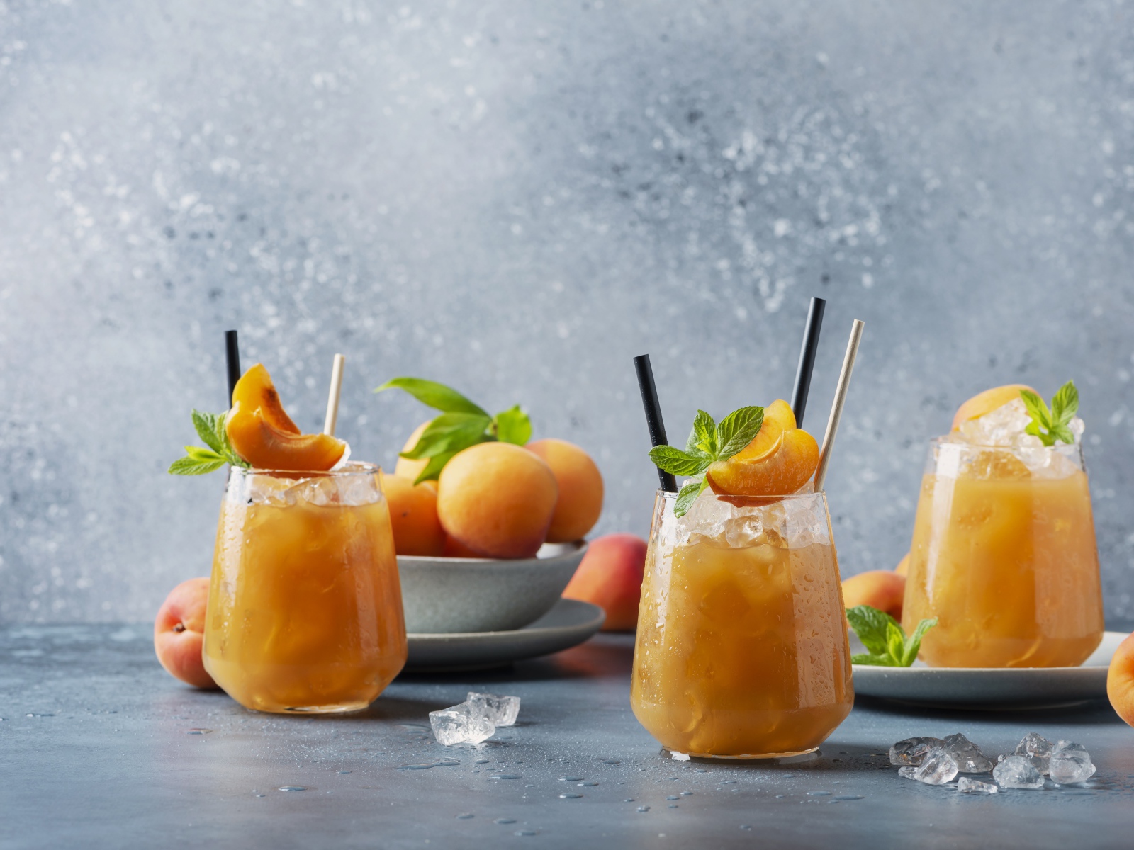 Холодный абрикосовый напиток со льдом в стаканах на столе со свежими абрикосами