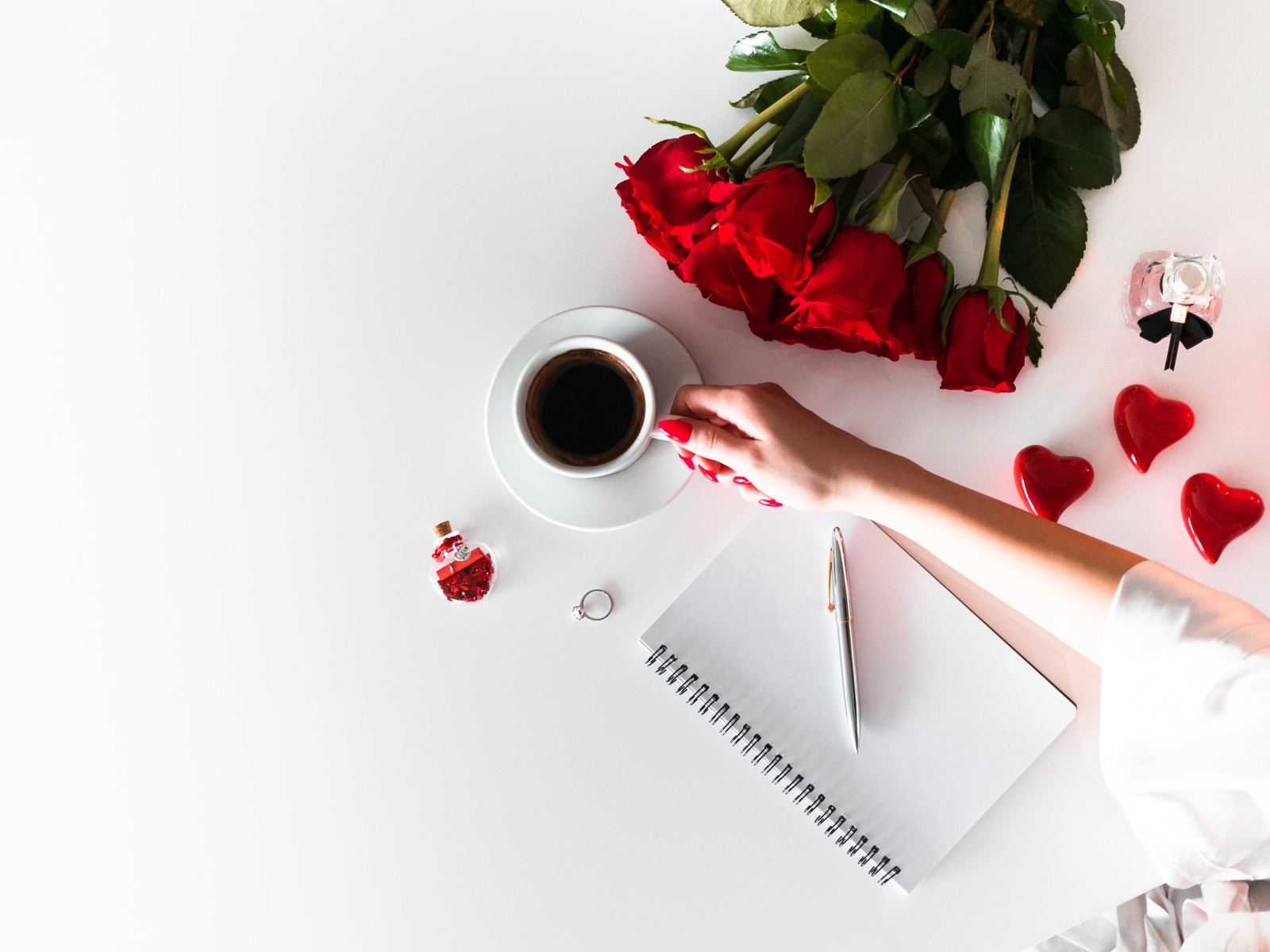 Девушка держит в руках чашку кофе на столе с блокнотом и букетом роз 