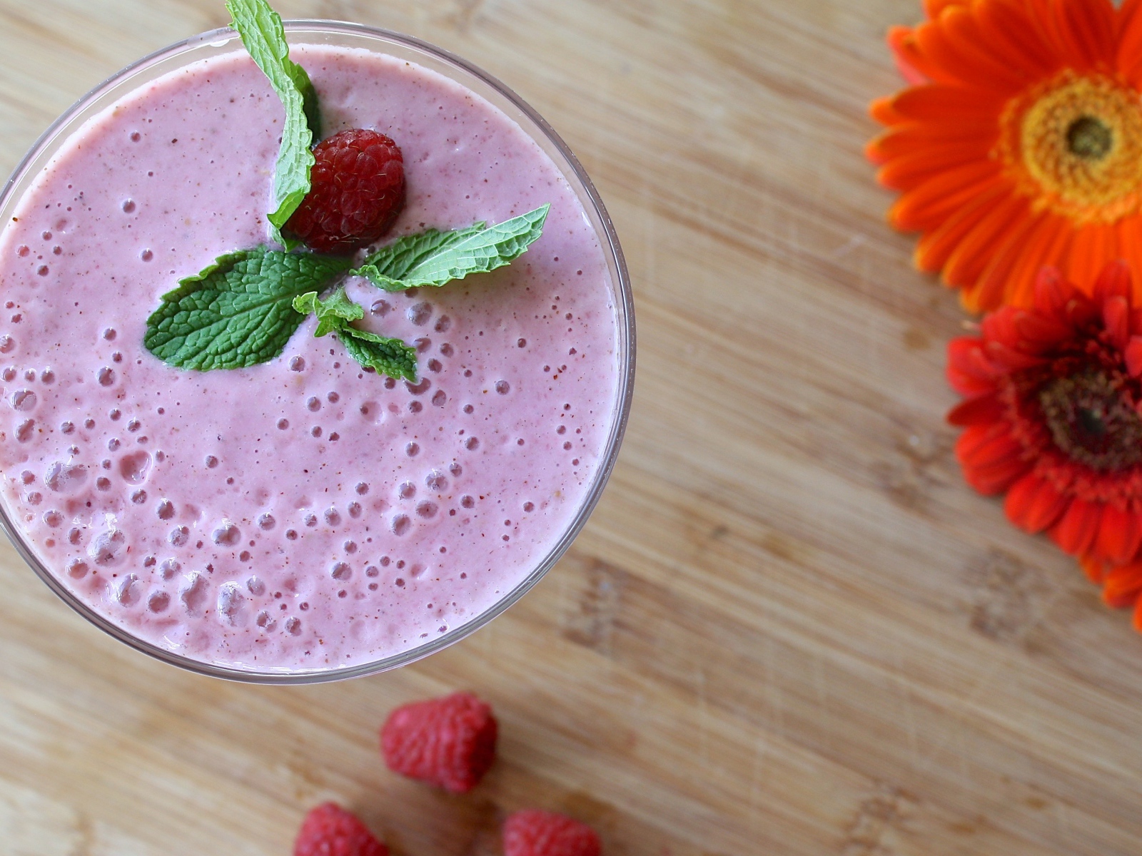 Малиновый смузи в стакане на столе с герберами