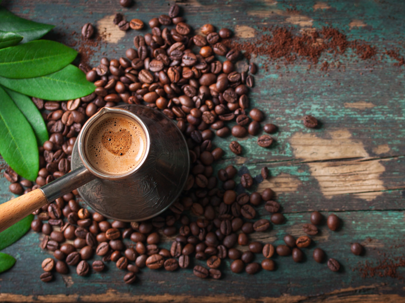 Турка с кофе на столе с зернами и зелеными листьями
