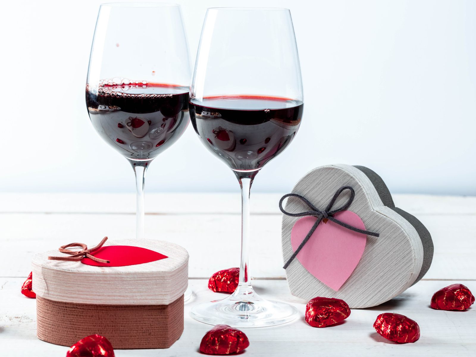 Две коробки с конфетами в форме сердца на столе с бокалами 