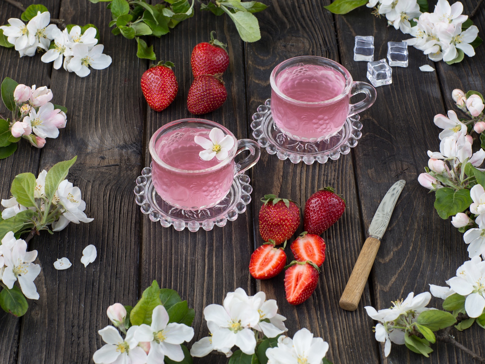 Две стеклянные чашки ягодного чая на столе с клубникой и цветами яблони