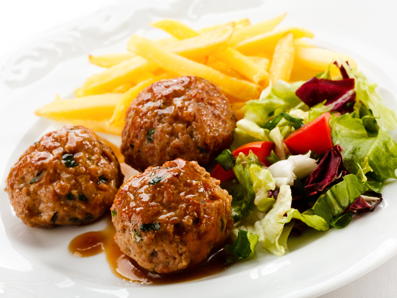 Фрикадельки с салатом и картофелем фри на белой тарелке