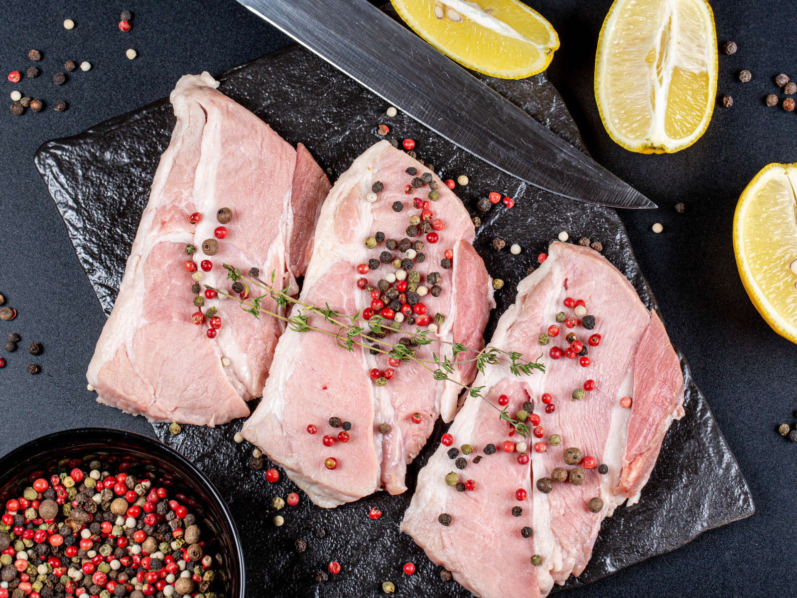 Куски свежего мяса на столе с зернами перца и лимоном
