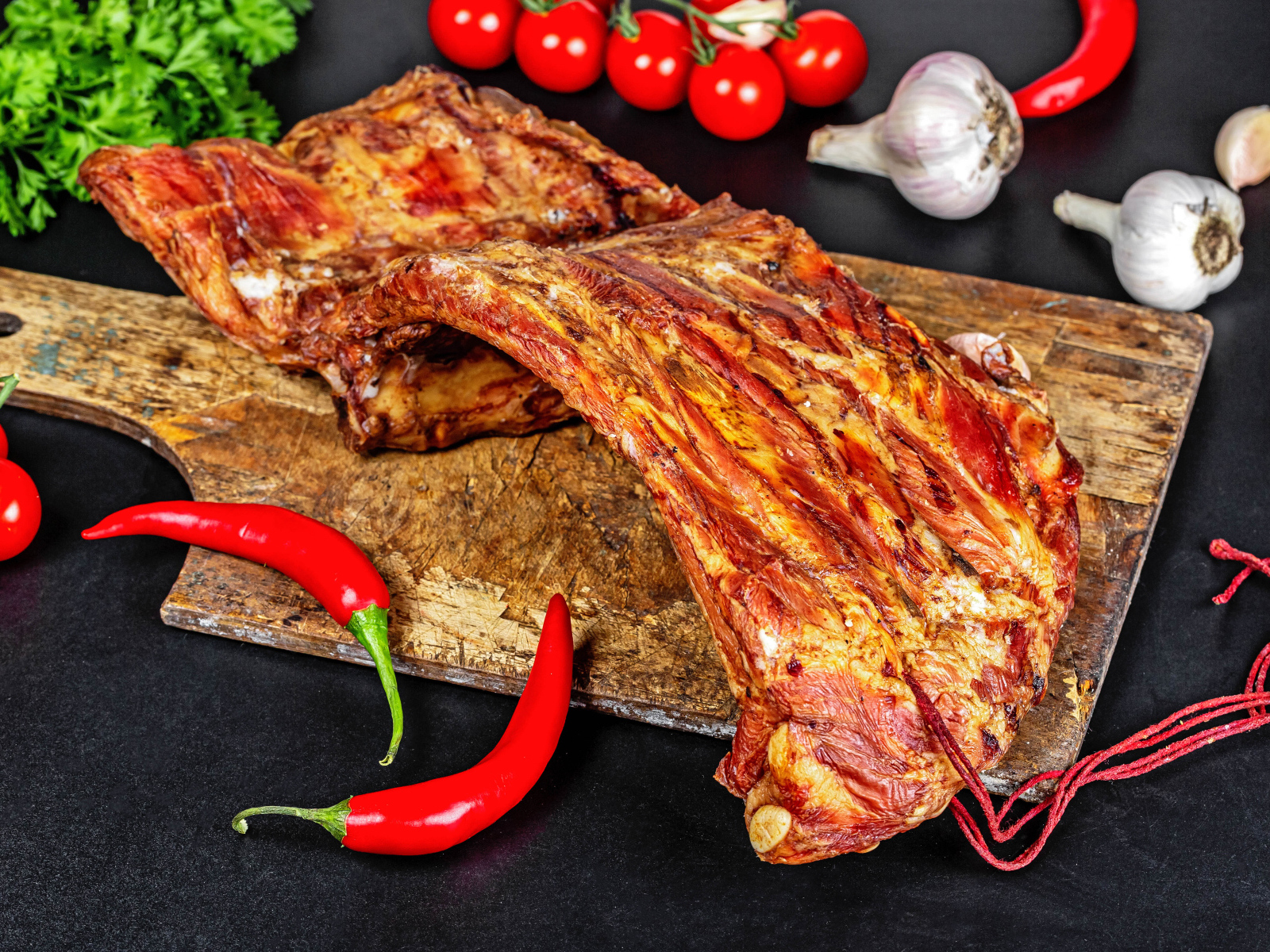 Копченые ребра на столе с красным перцем, чесноком и помидорами