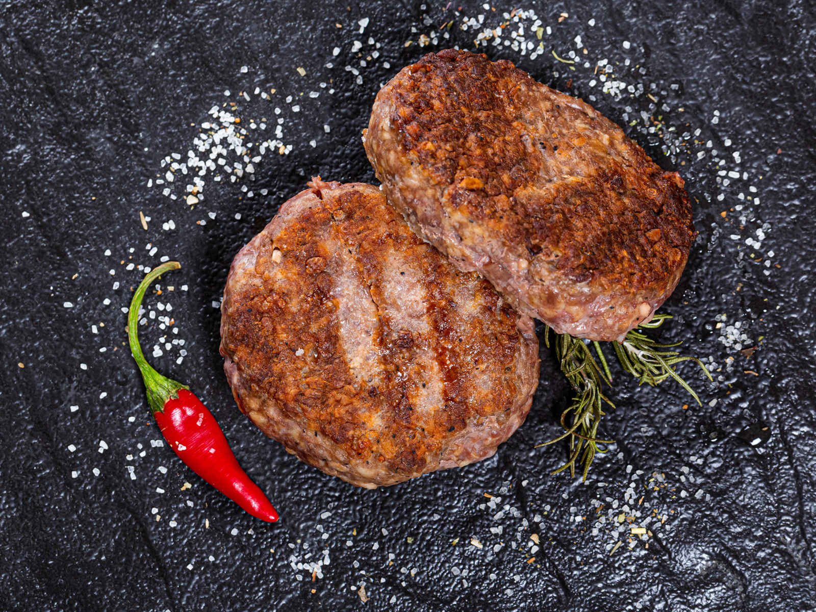 Две котлеты на черной поверхности с красным перцем