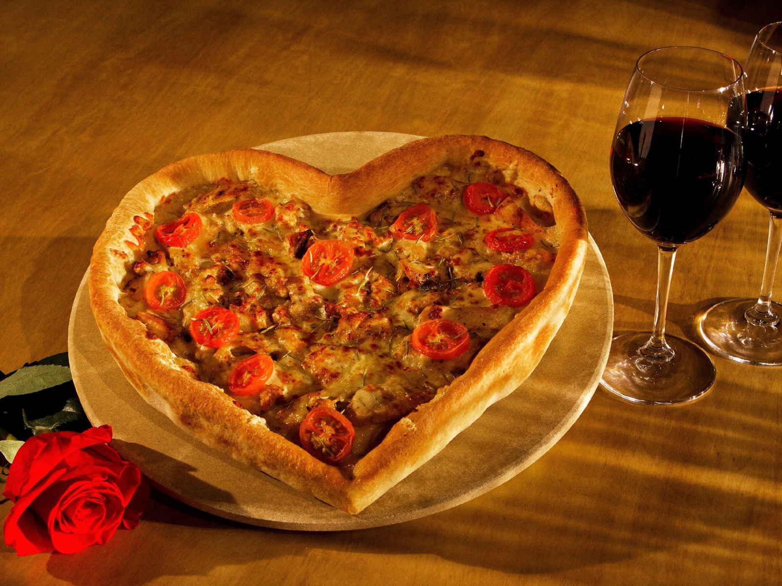 Heart-shaped pizza on a table with a rose and two glasses of wine