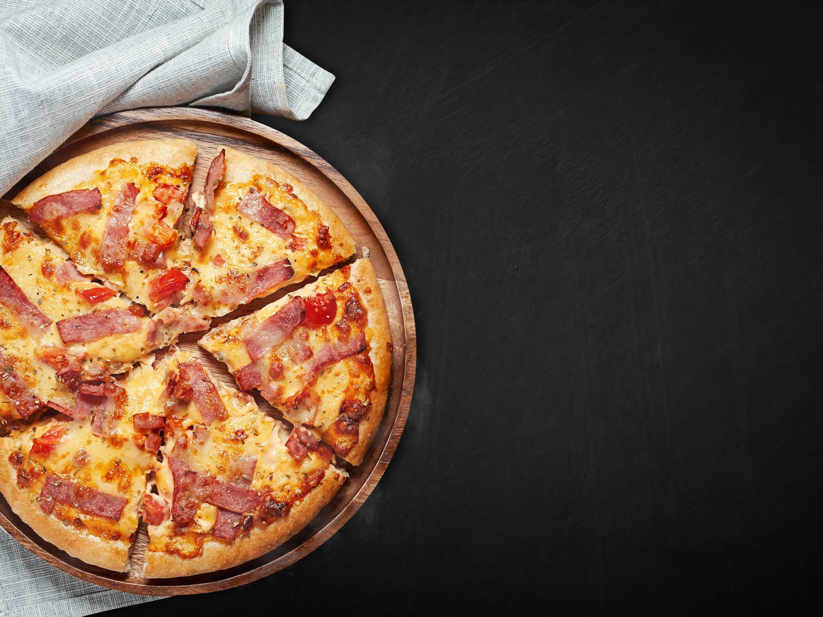 Пицца с кусочками бекона на доске на черном фоне