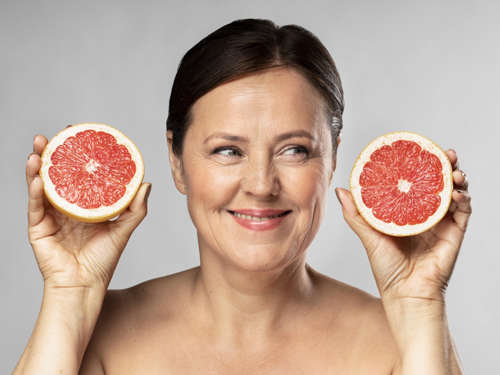 Улыбающаяся женщина с грепфрутом в руках на сером фоне