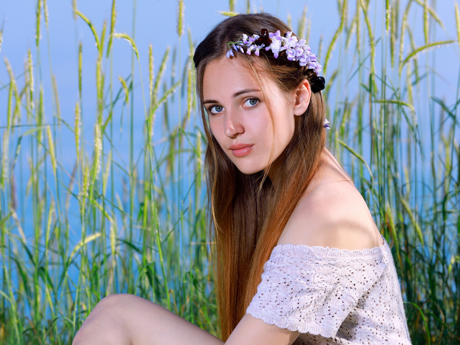 Красивая молодая девушка с венком на голове сидит на поле с колосьями 