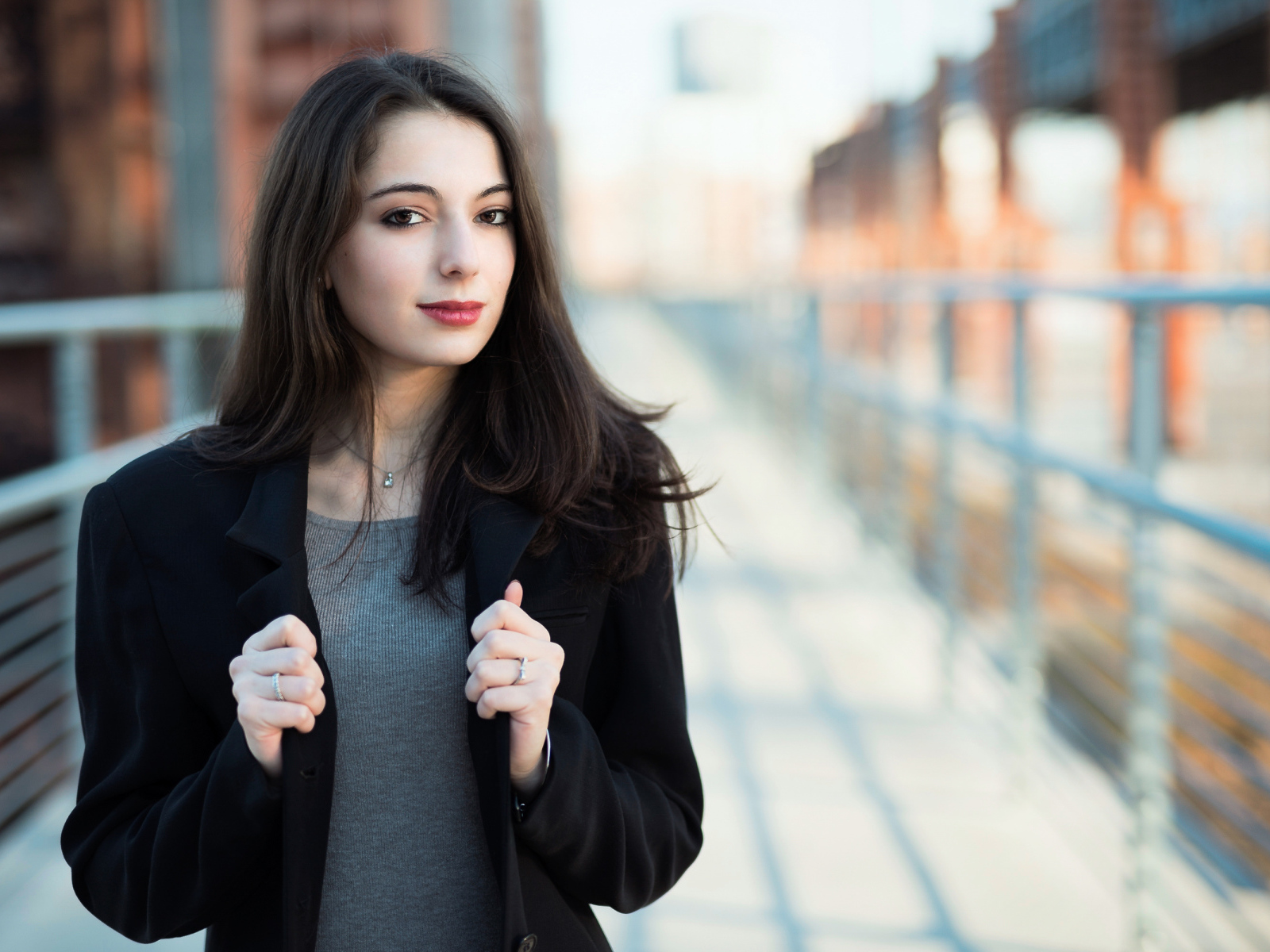 Молодая девушка в черном пальто стоит на мосту