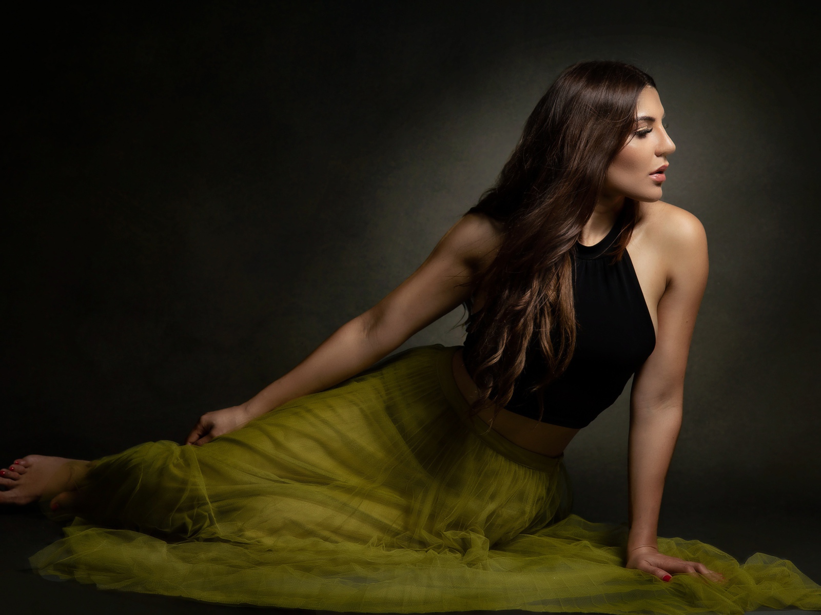 Молодая девушка в длинной юбке сидит на полу