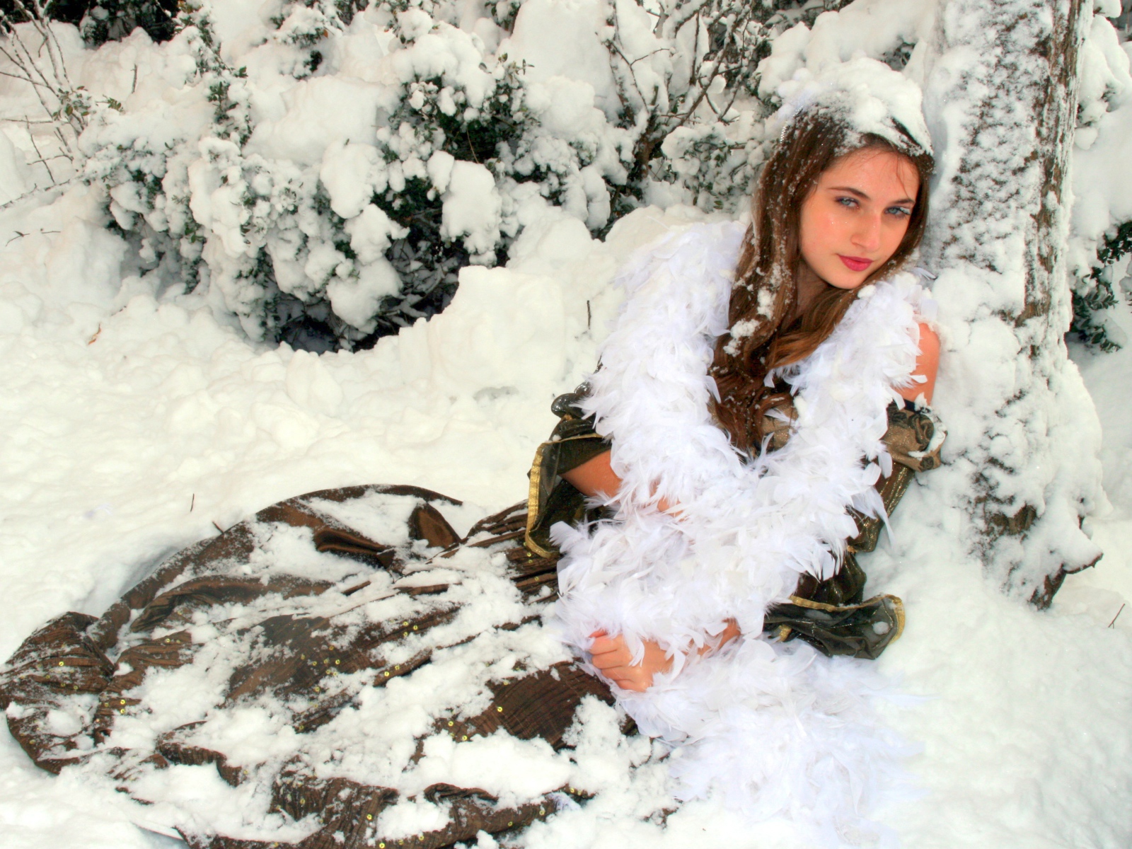 Молодая девушка сидит на снегу под елью 