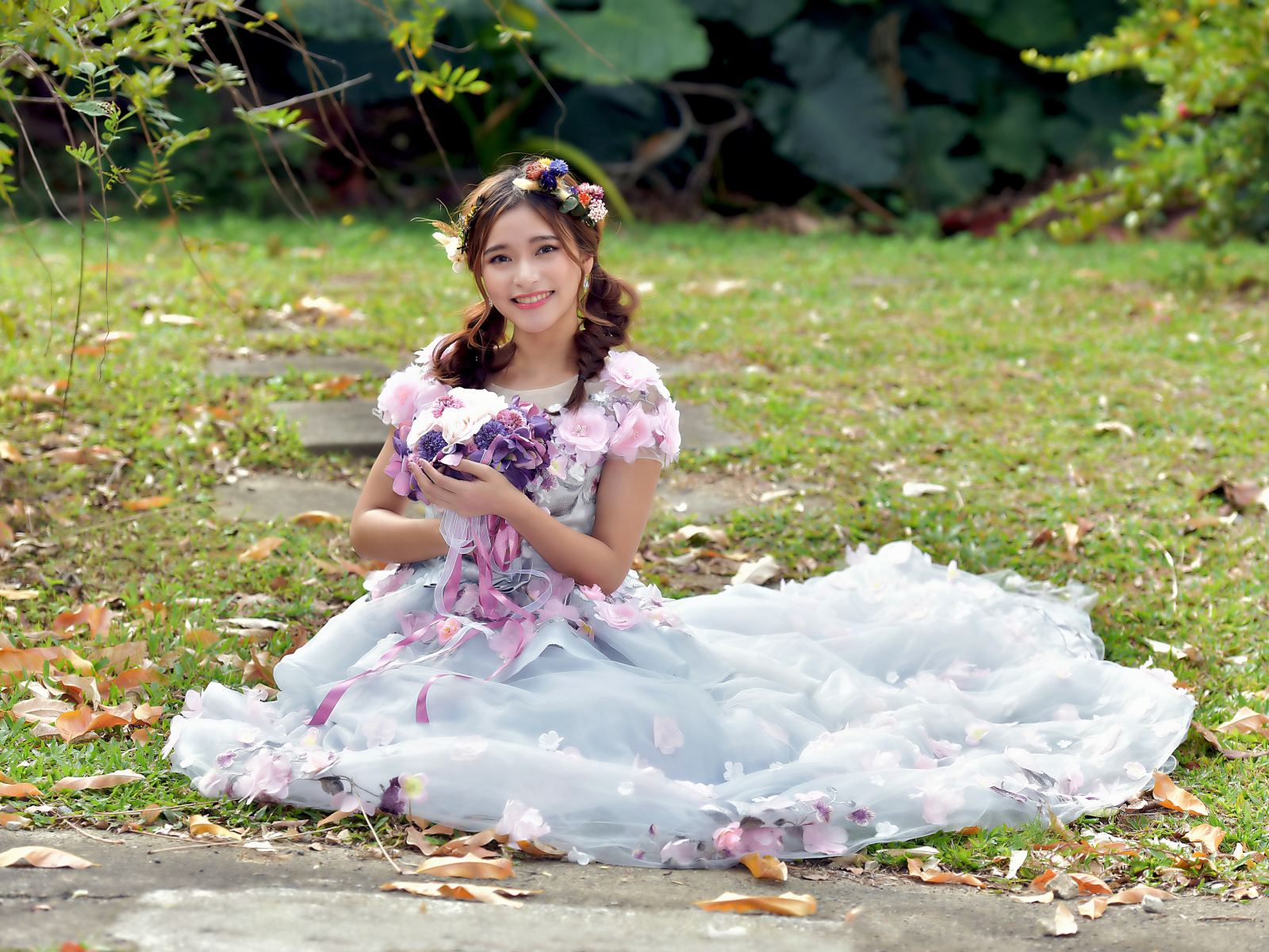 Девушка азиатка в красивом платье сидит на земле с букетом 