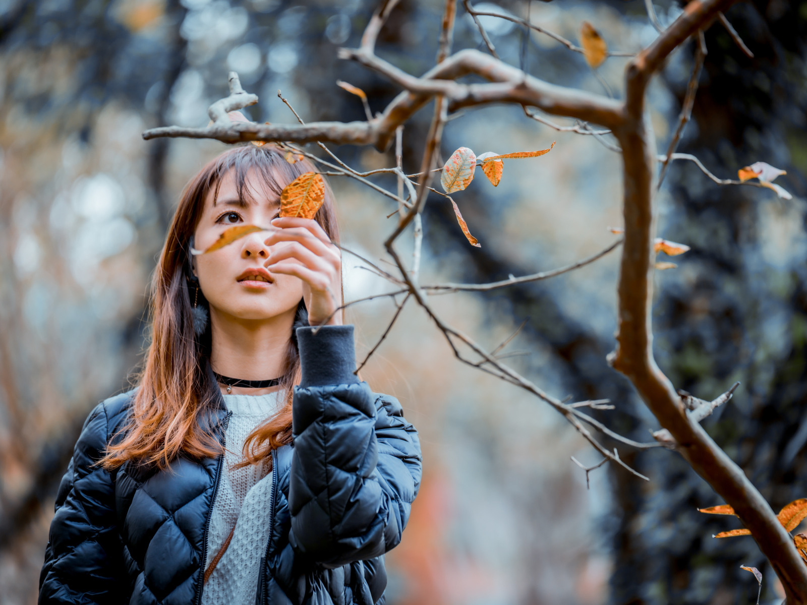 Девушка азиатка в черной куртке у дерева
