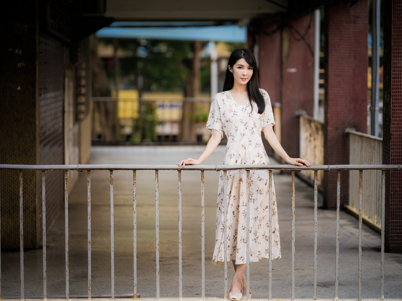 Красивая азиатка в платье стоит у перил