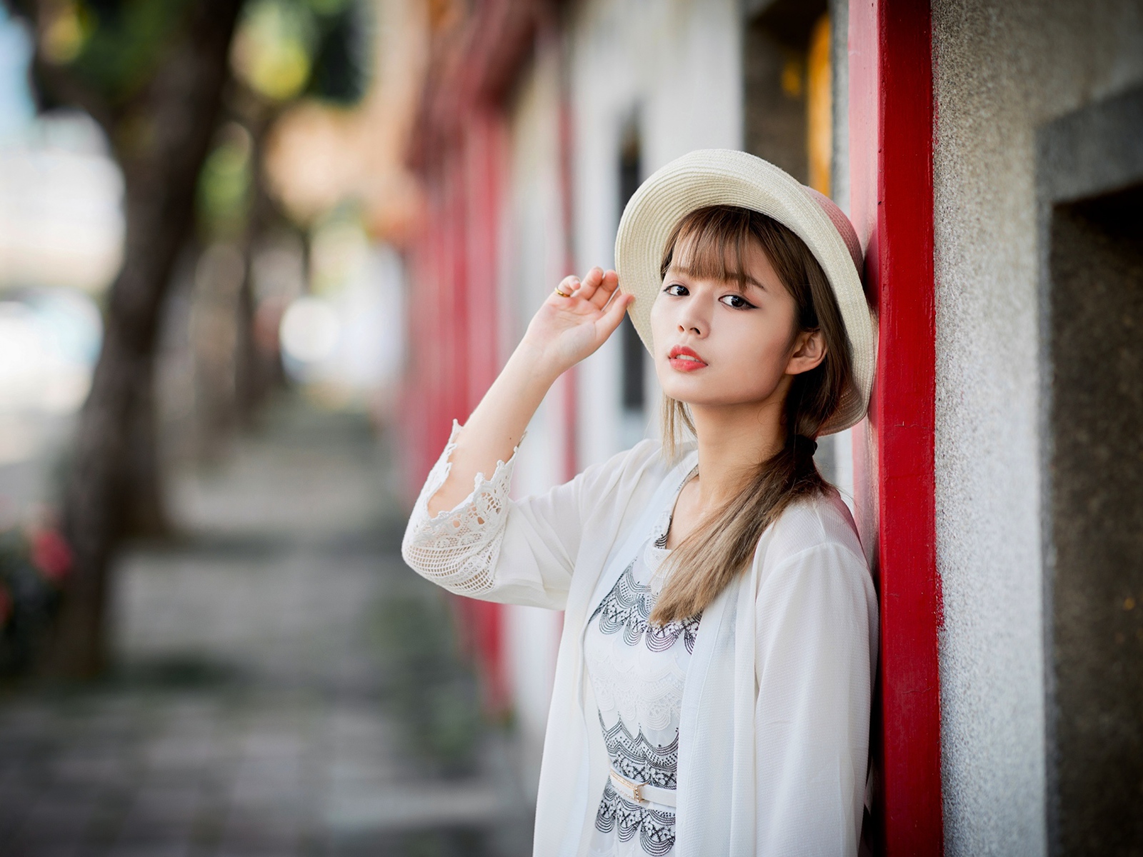 Красивая азиатка в шляпе стоит у стены