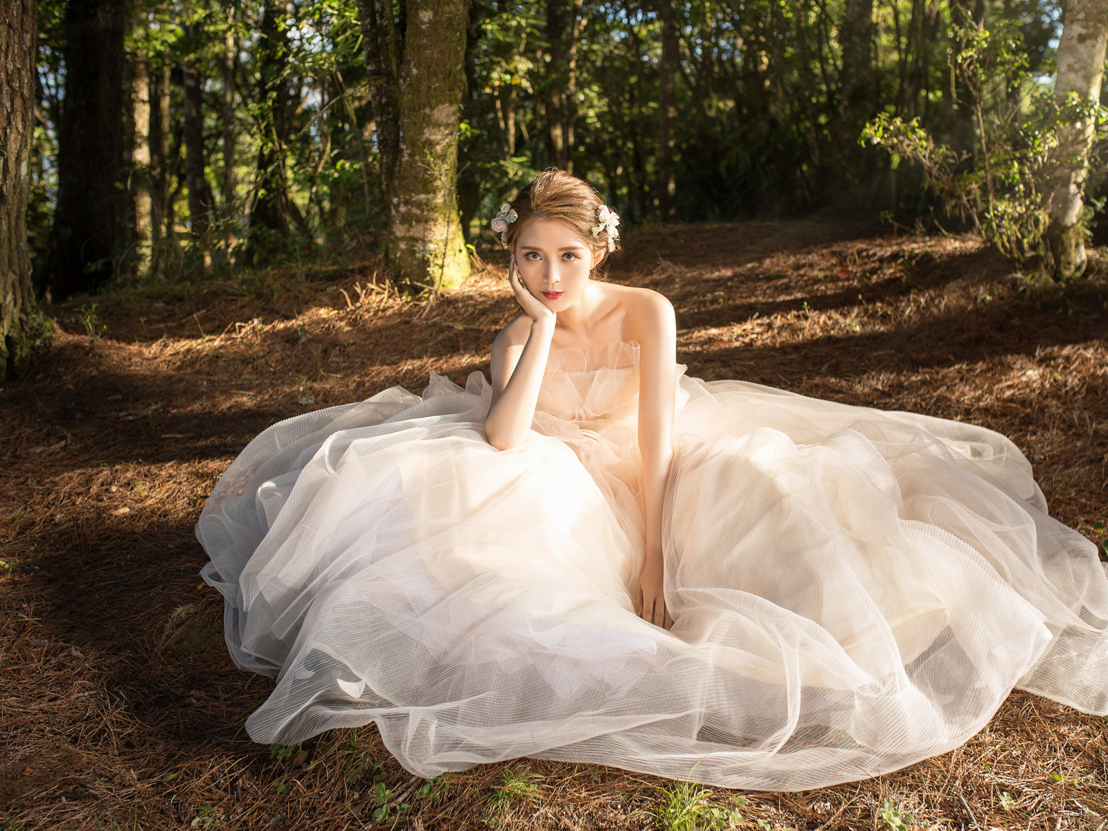 Красивая девушка азиатка в белом свадебном платье сидит на земле