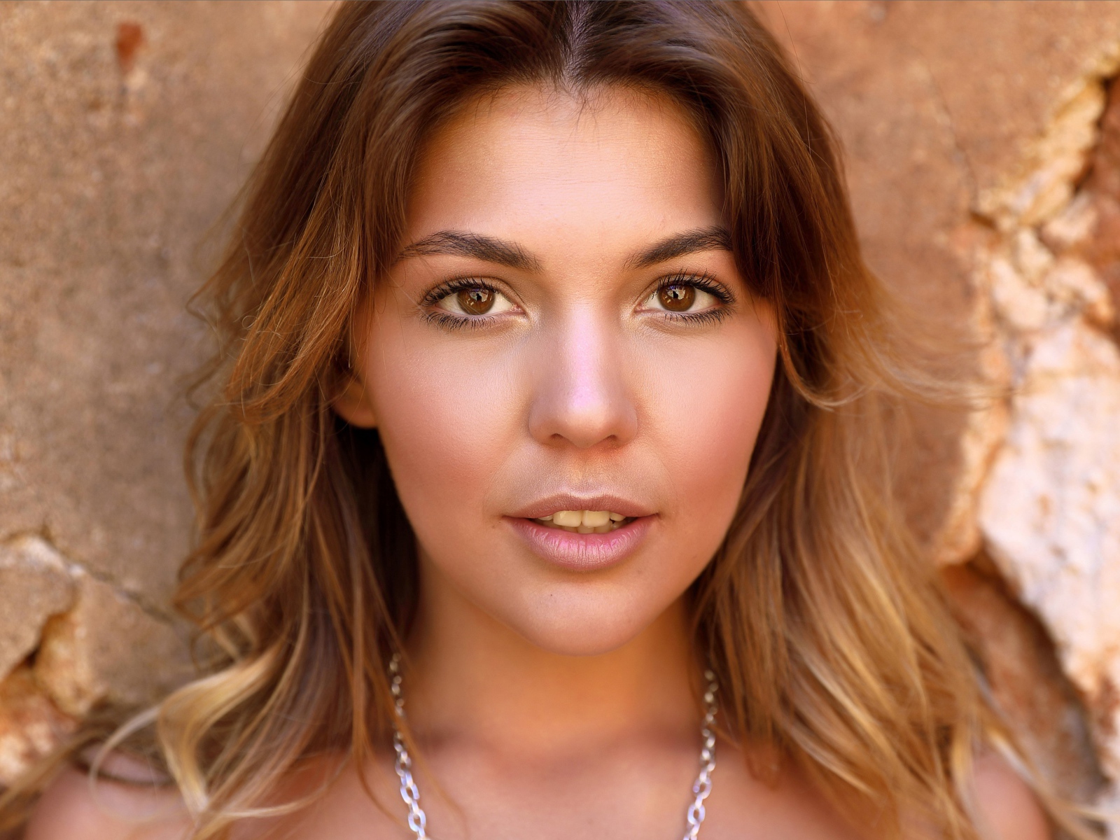 Красивая кареглазая девушка стоит у стены 