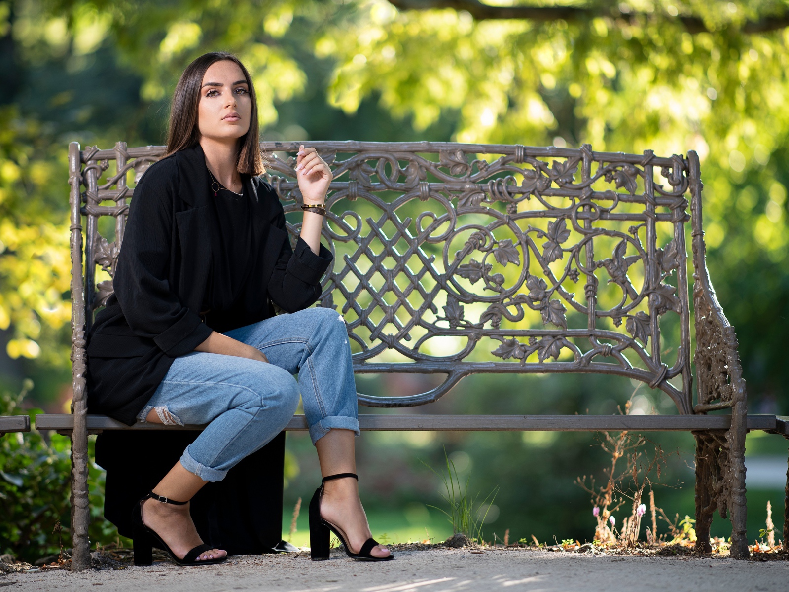 Красивая девушка в черном пальто сидит на лавочке в парке
