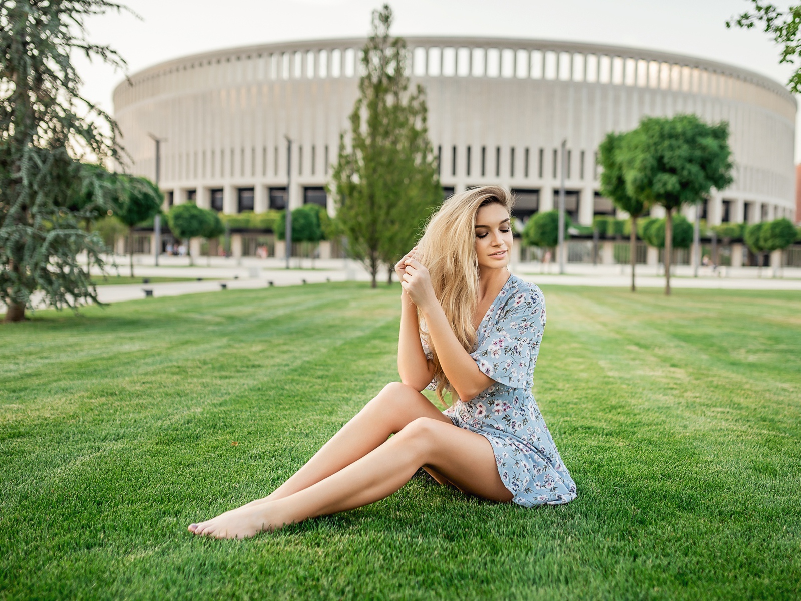 Красивая девушка в платье сидит на зеленом газоне 