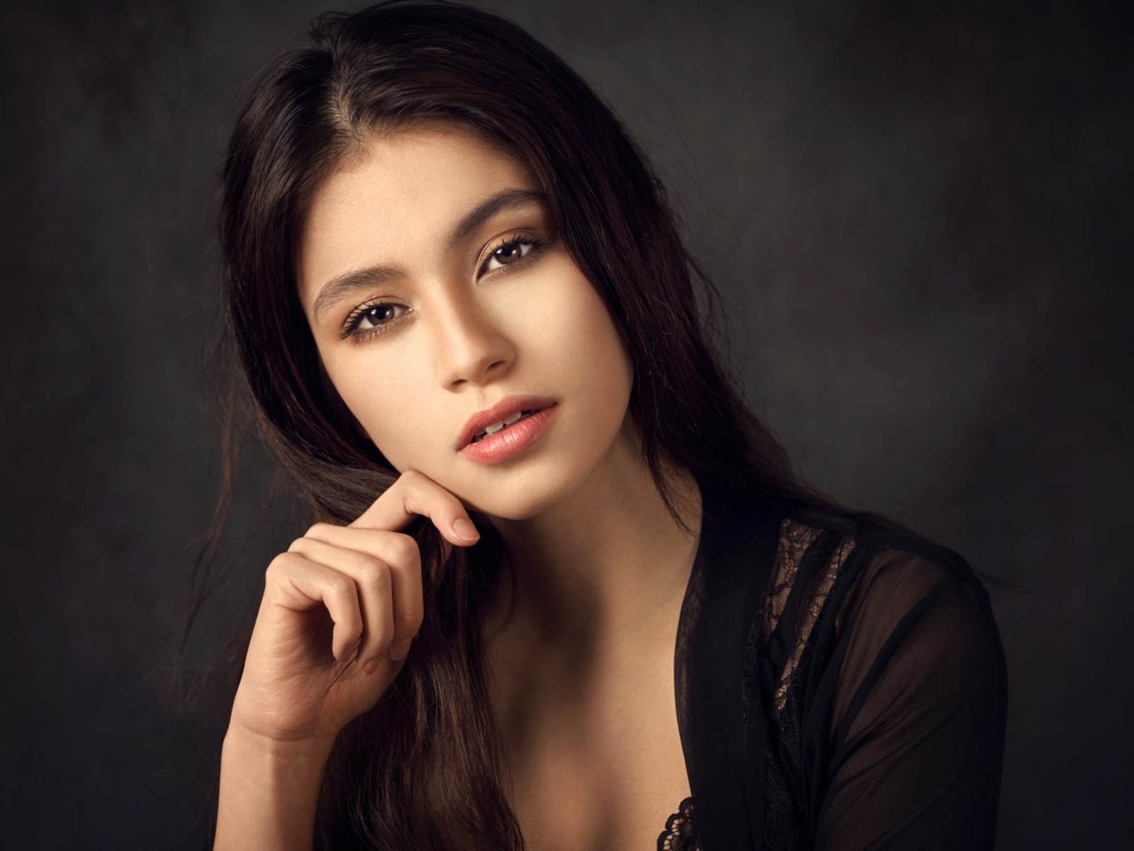 Красивая девушка в черном сидит на сером фоне