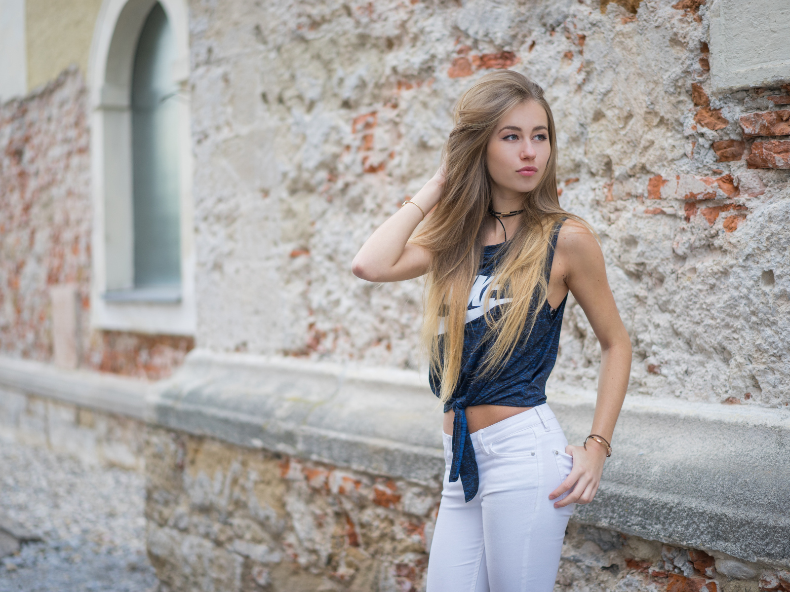 Красивая девушка в белых брюках стоит у стены 