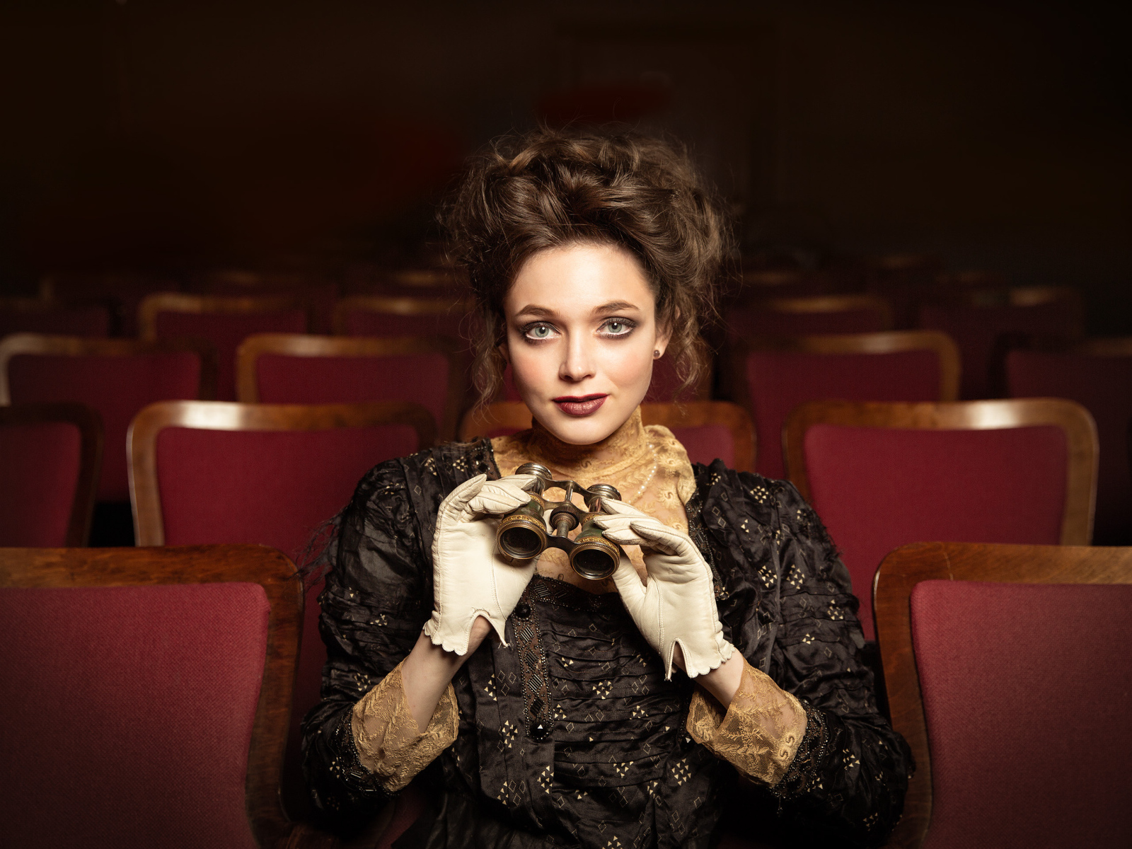 Красивая девушка с биноклем сидит в театре