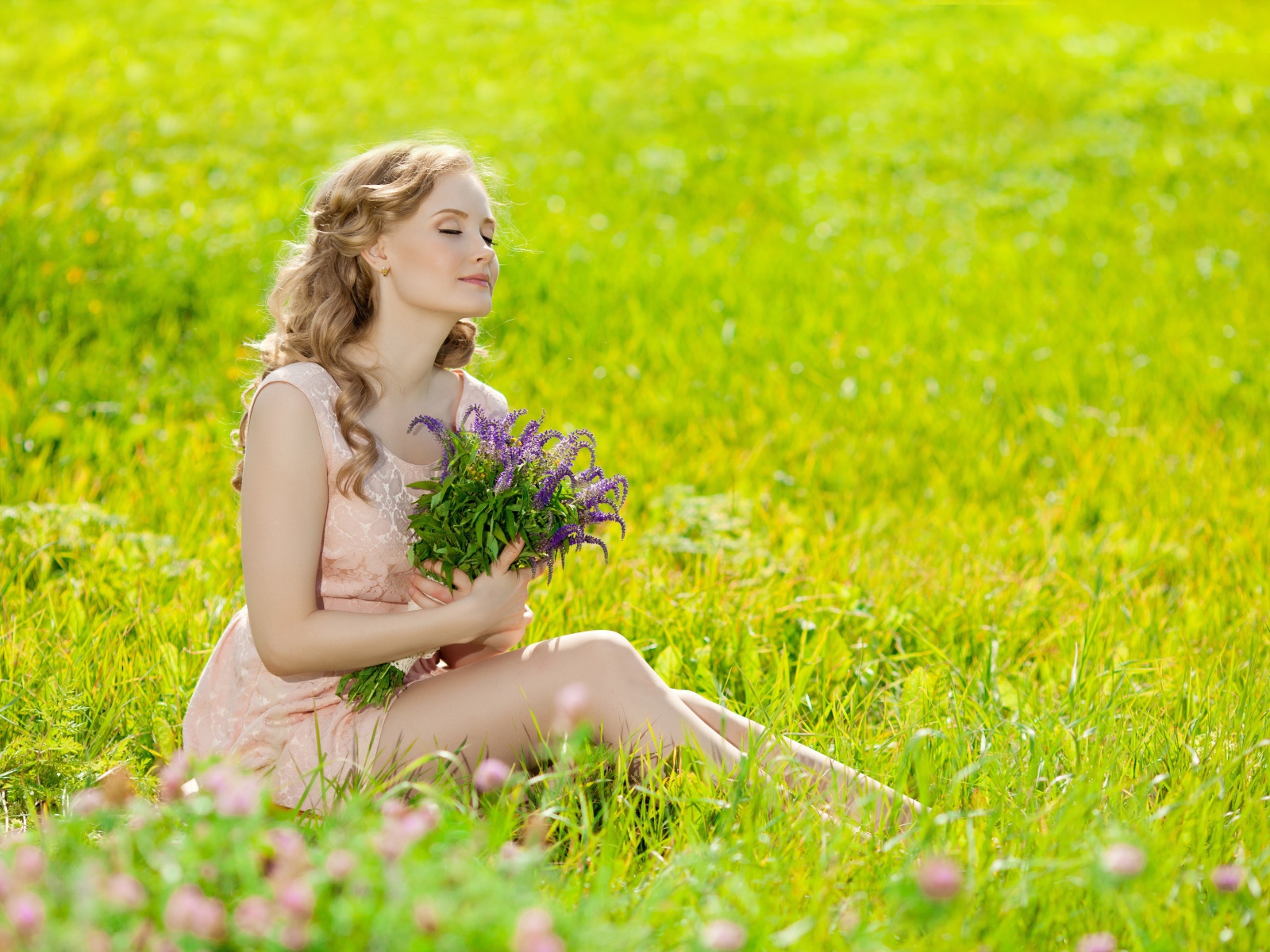 Красивая молодая девушка с букетом цветов сидит на зеленой траве