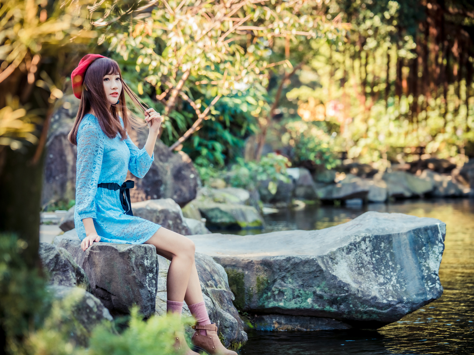 Милая азиатка в берете и синем платье сидит у воды 