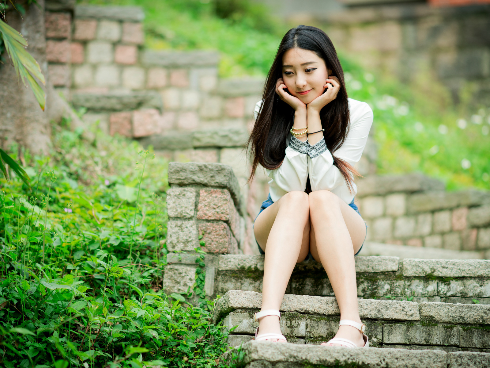 Мечтательная девушка азиатка сидит на ступеньках 