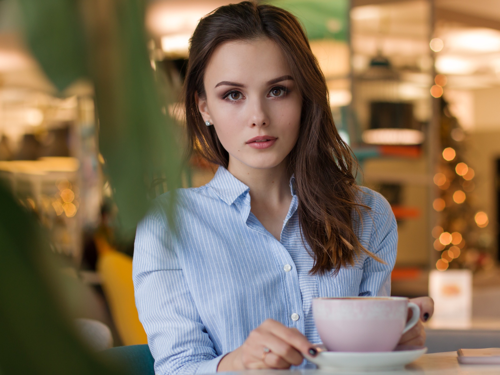 Девушка в голубой рубашке с чашкой кофе на столе в кафе