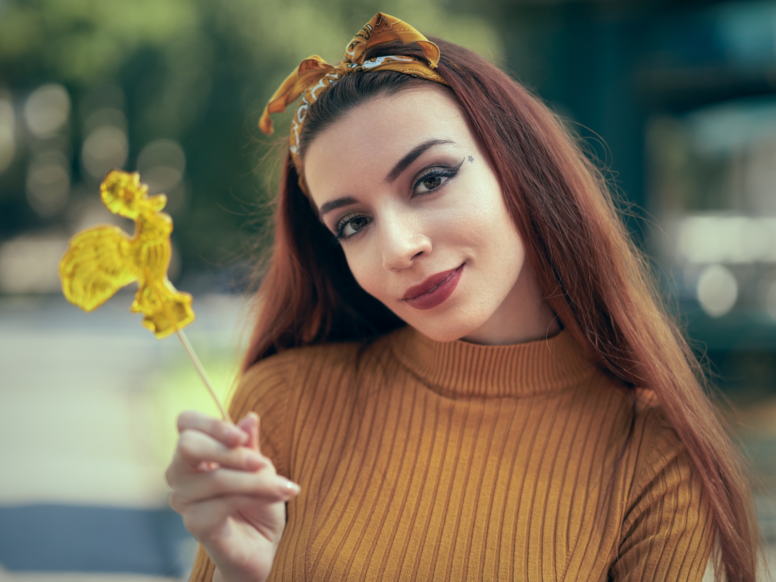 Длинноволосая девушка в свитере с леденцом в руке