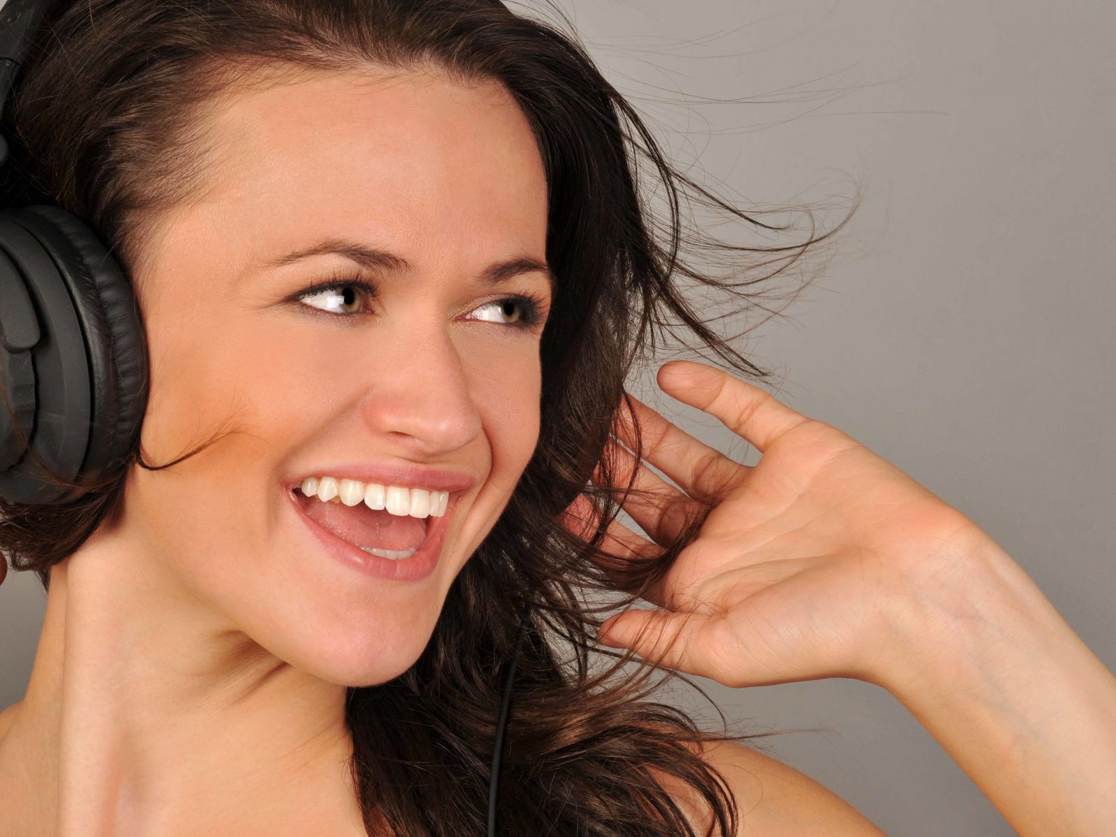 Улыбающаяся девушка в наушниках на сером фоне 