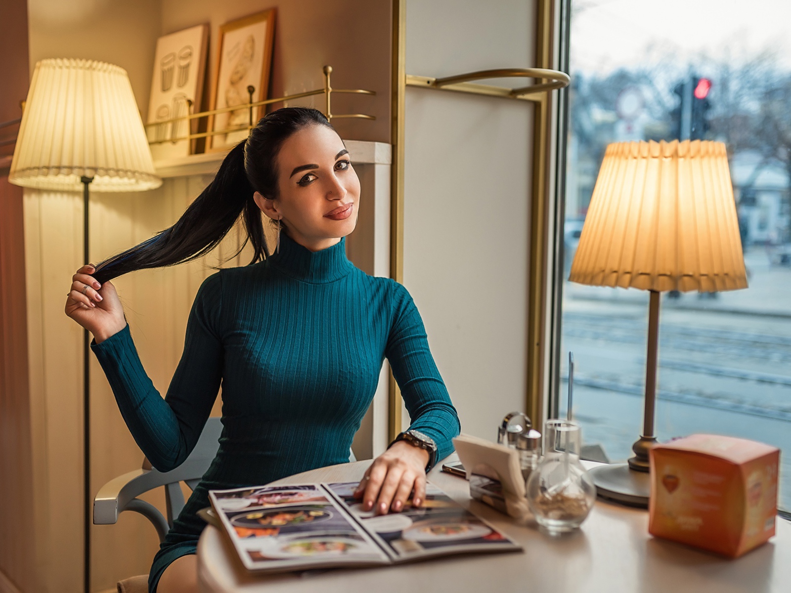 Стильная девушка в платье сидит в кафе у окна