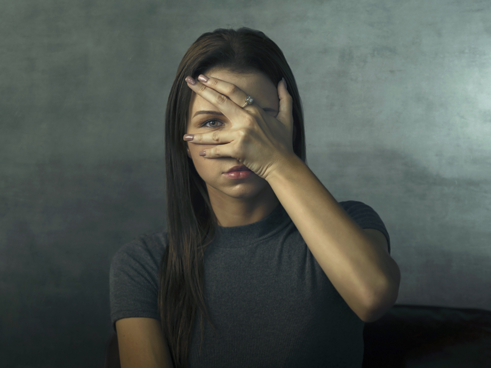 Молодая девушка закрыла лицо рукой на сером фоне
