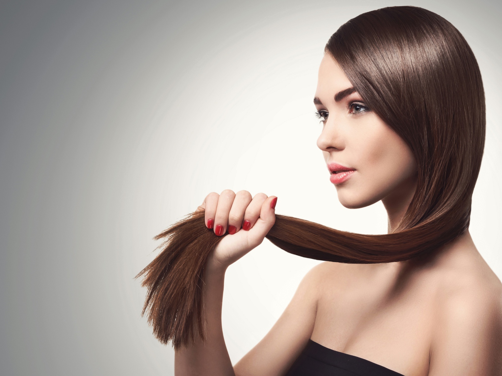 Молодая девушка держит в руках волосы на сером фоне